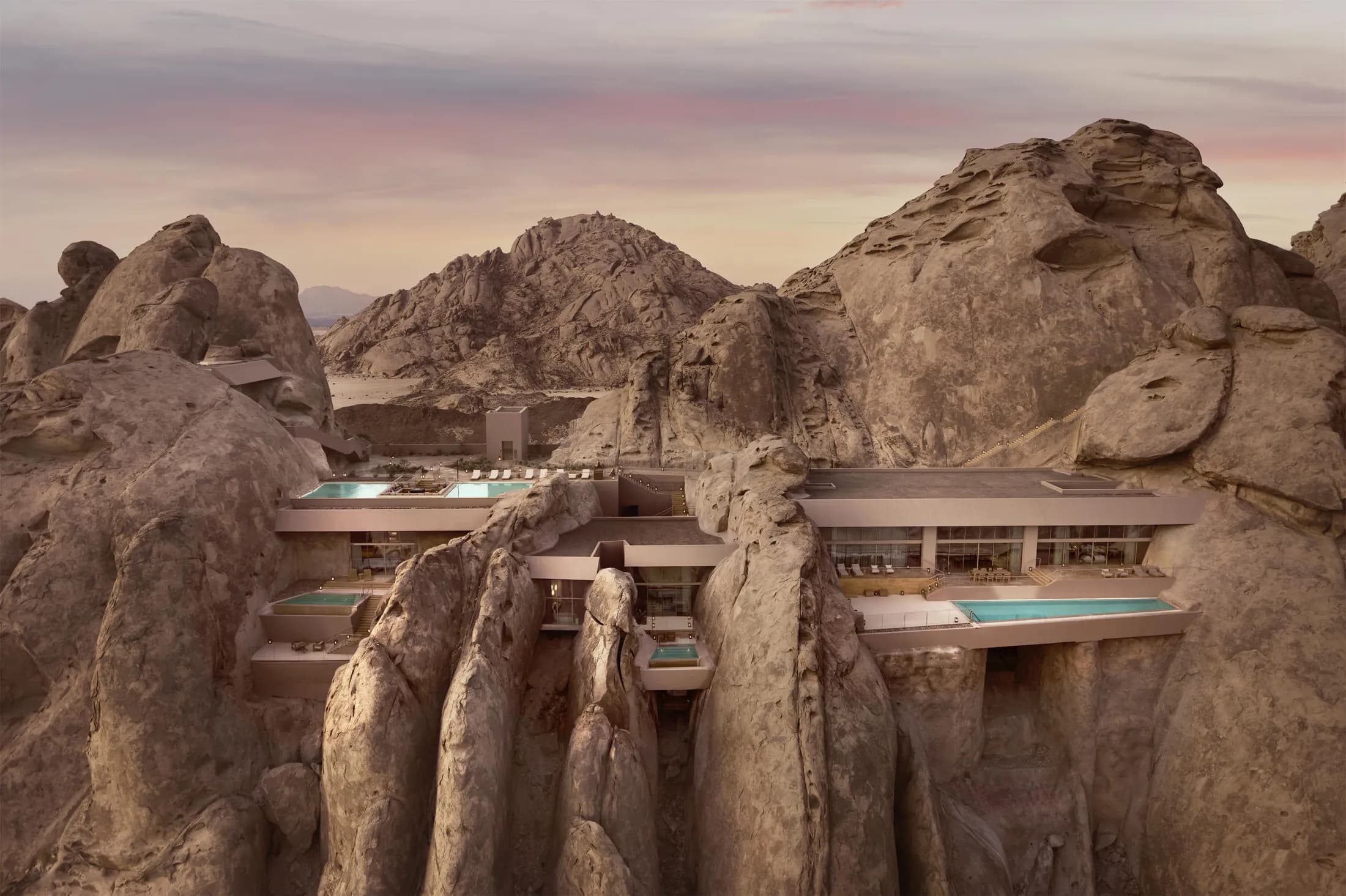 An aerial view of a resort set into towering desert boulders, infinity pools tucked between the rock at dusk.