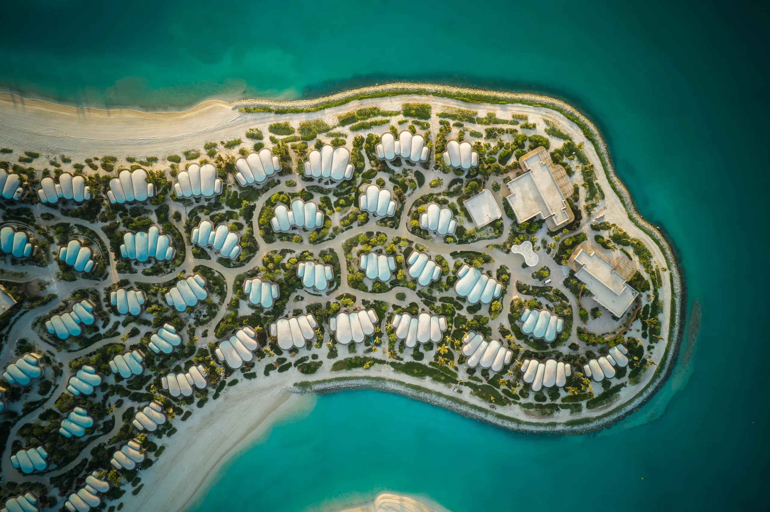 Aerial view of Shura Island's shell-roofed villas threaded through restored landscape.